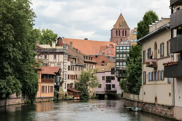 Half-timbered houses along a canal in the Petite France quarter of Strasbourg, under a church tower.
