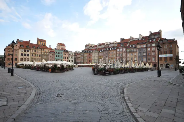 The cobbled Old Town Market Place in Warsaw, with café umbrellas in front of tall painted houses.