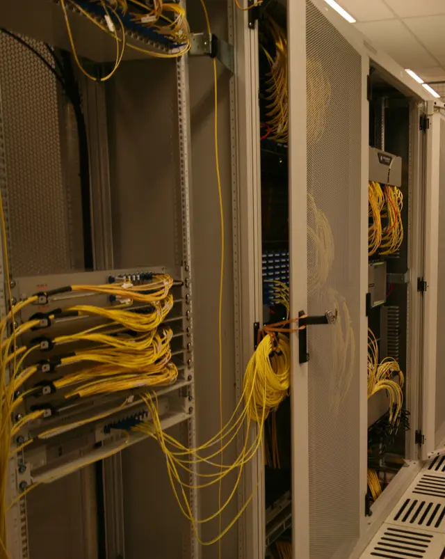 Racks in an internet exchange's core cage, their doors open, yellow fibre cables looping between patch panels.